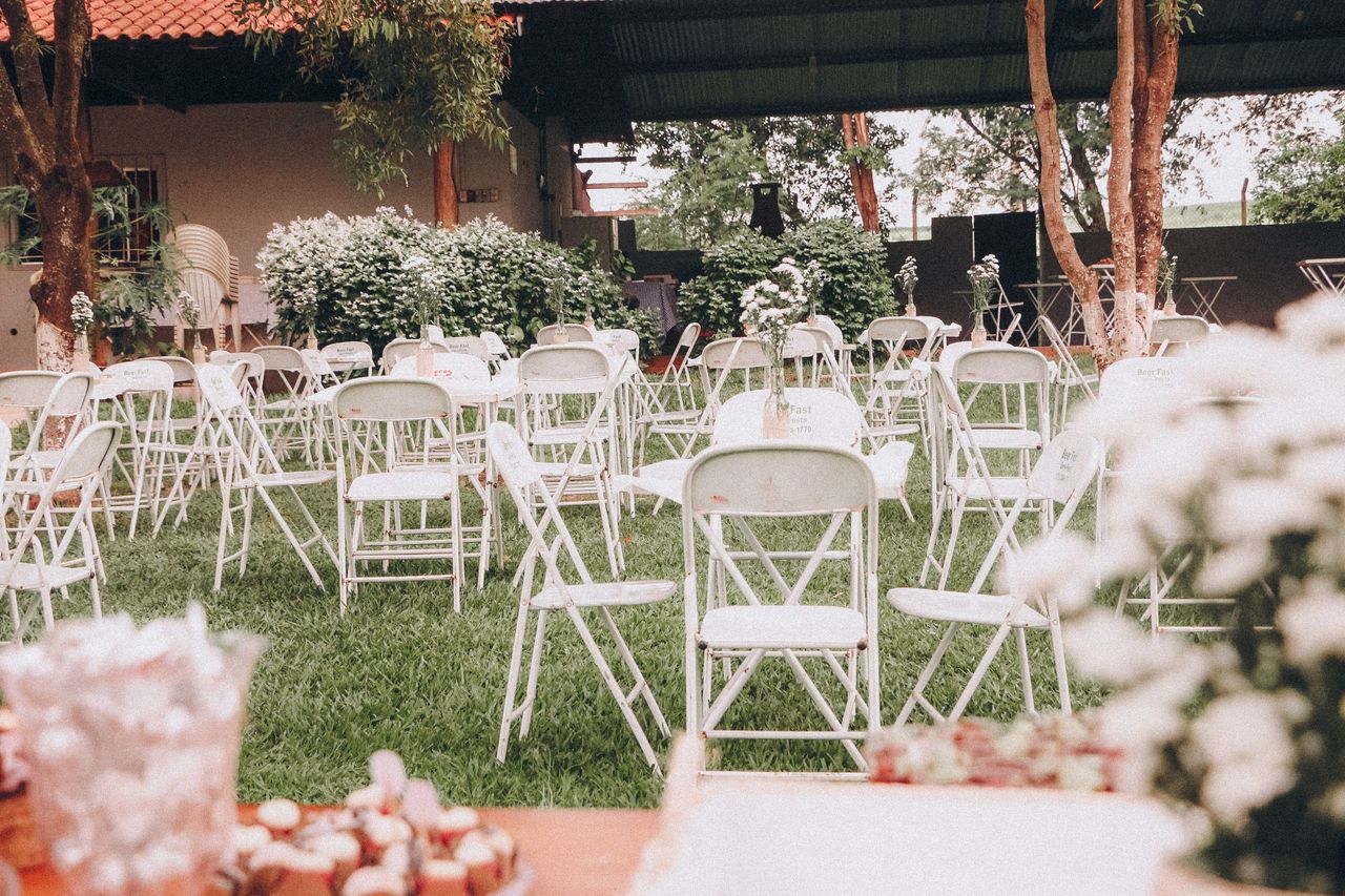 who-we-are An outdoor wedding venue setup with white folding chairs on green grass and decorative plants.